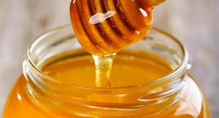 honey dripping off of honey stick into jar