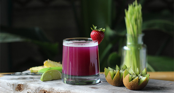 glass of purple juice with limes, strawberries and kiwi